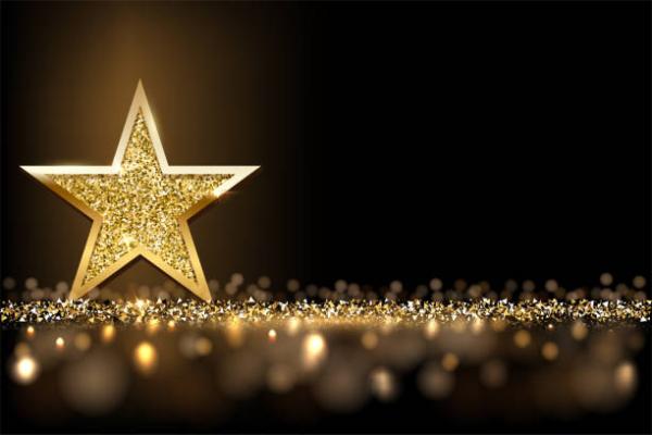 A gold star, with five points, smooth edges, and a textured centre. Gold flakes are at its base.