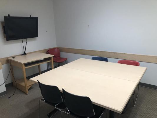 Group study room. Rooms described below. The image shows two tables put together to create a square. Four chairs at desk and four chairs stacked in corner.