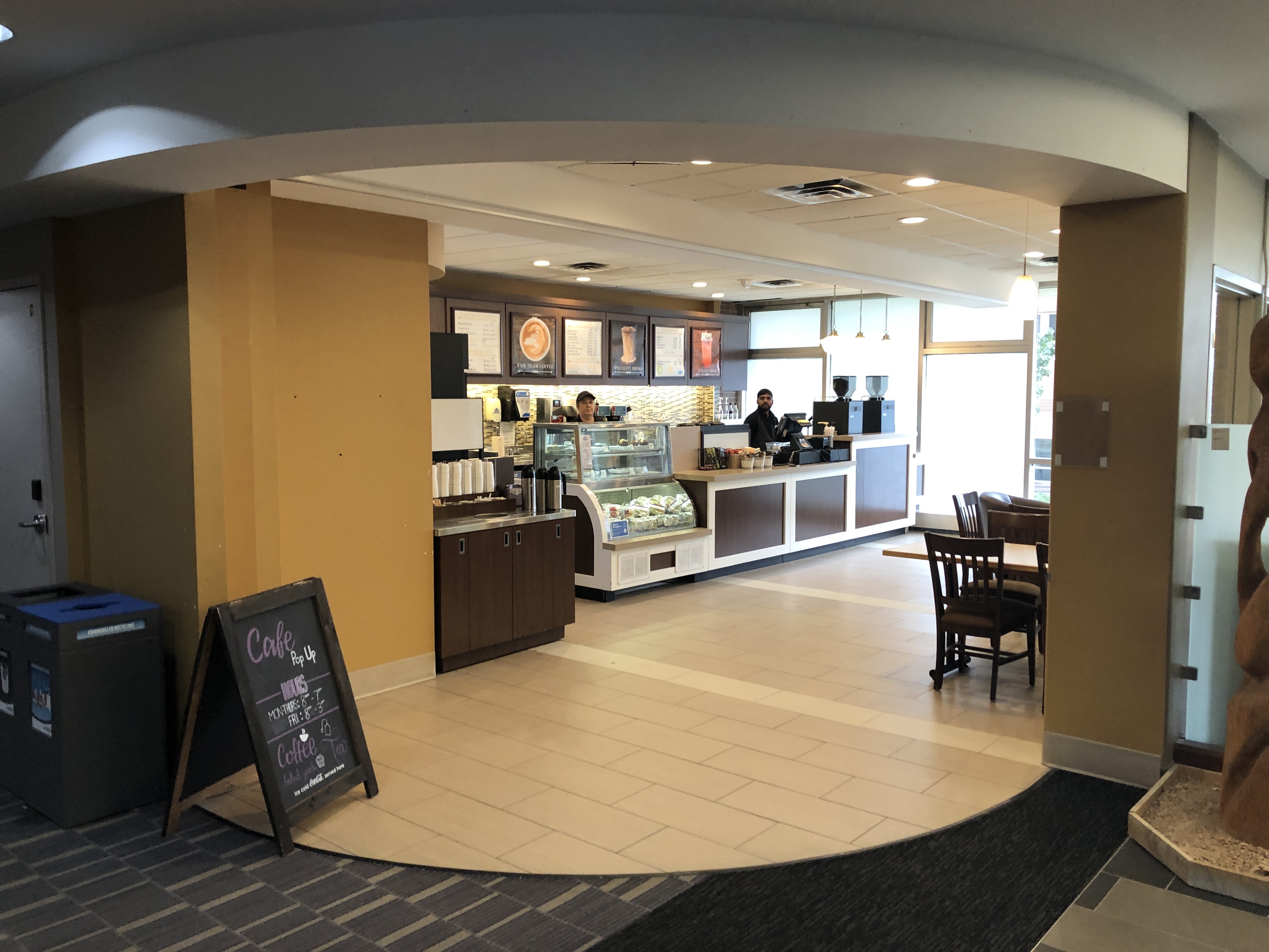 Coffee shop when it is open. There is a sandwich board with hours. The floor of the coffee shop is titled while the lobby is carpeted. There is a counter to order and usually two employees. There are chairs and a few tables