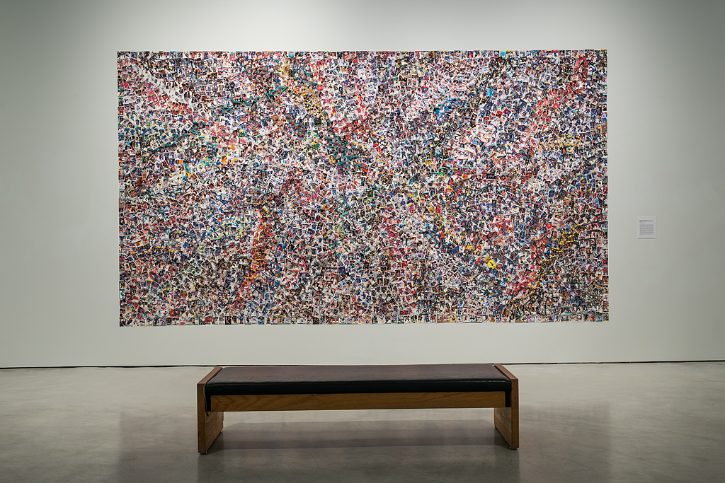 Exhibition installation photograph of a large rectangular abstract collage comprising over one thousand individual hockey cards. In front of the collage is a viewing bench