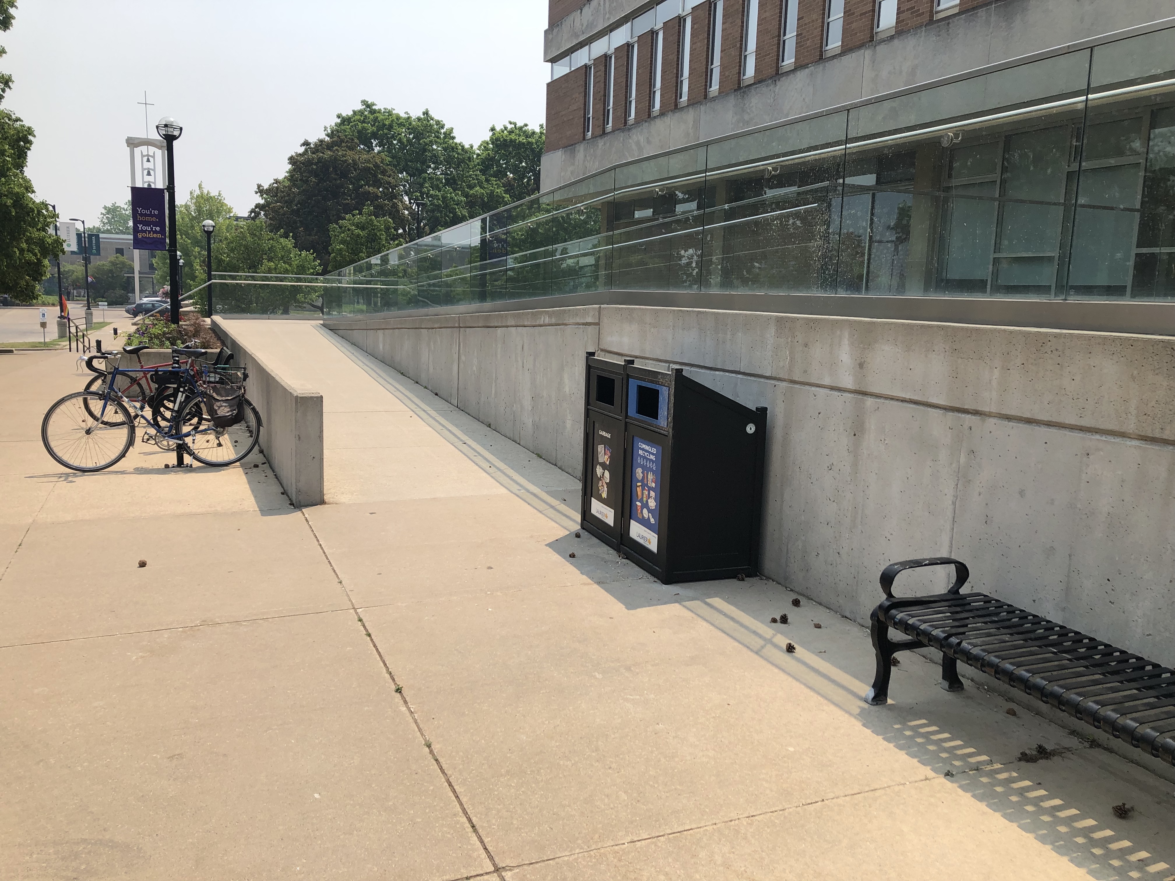 The ramp route. A bench, garbage and recycling containers are at the bottom of the ramp. The ramp leads to a mid-point, which turns around to a second ascending ramp.