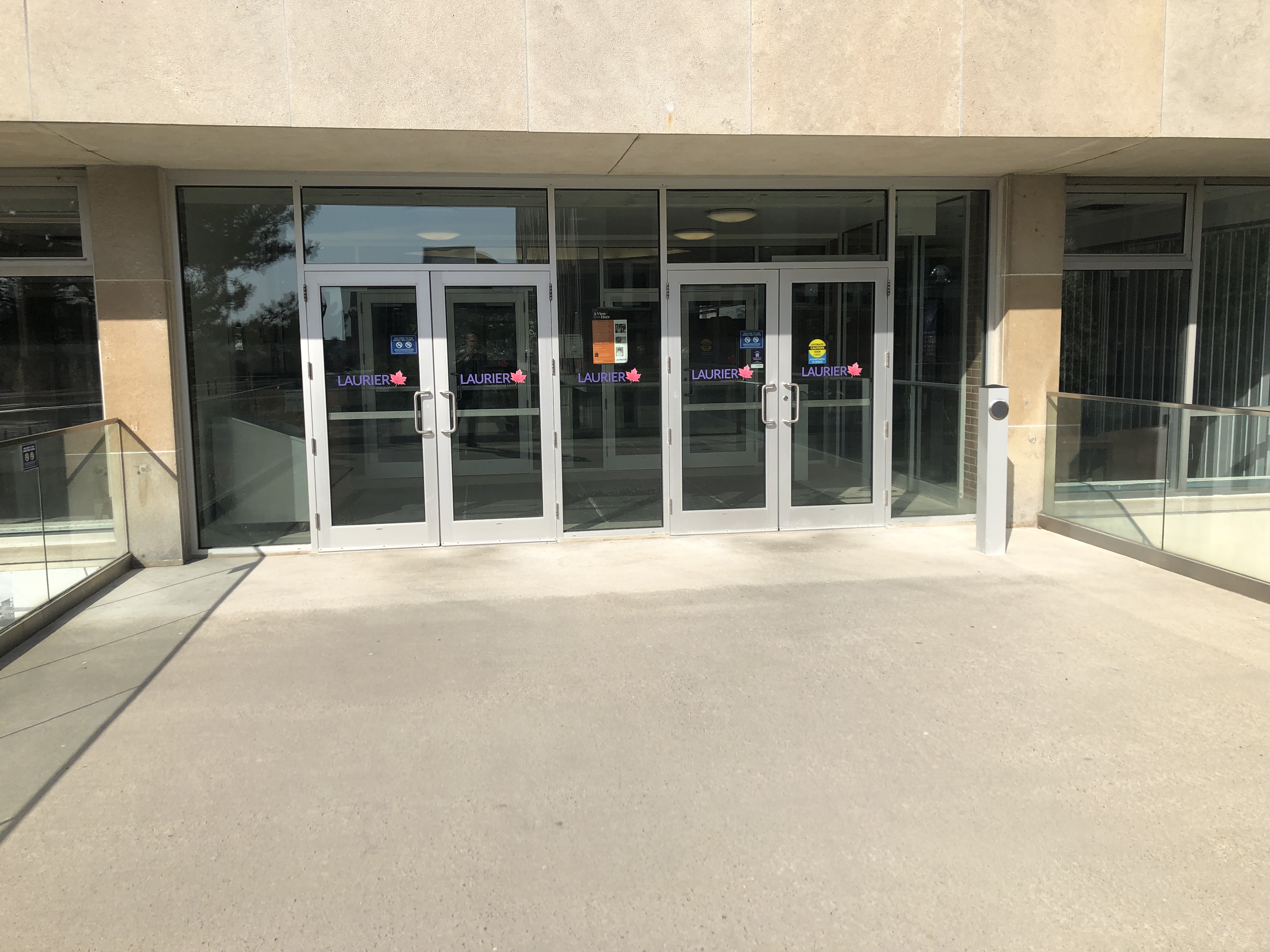Across the landing, which has hand rails on either side, are two sets of double doors to enter the library. Facing the library, on the right is a square bollard that has a round push button to open the doors automatically