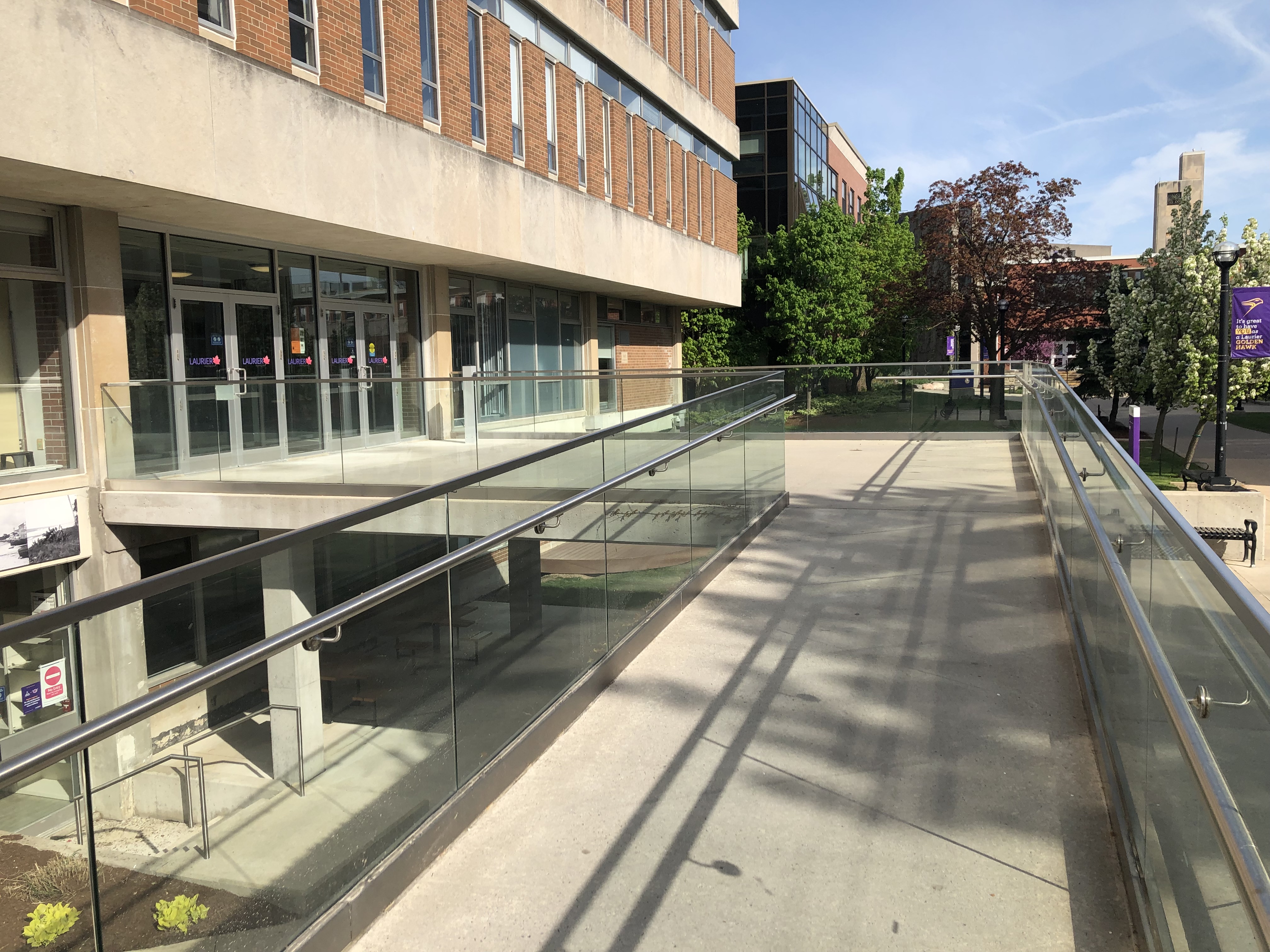 The second ascending ramp has hand rails along each side. It leads to a landing area. The landing area has a short walkway to the front doors of the library. The walkway has handrails along side of it.