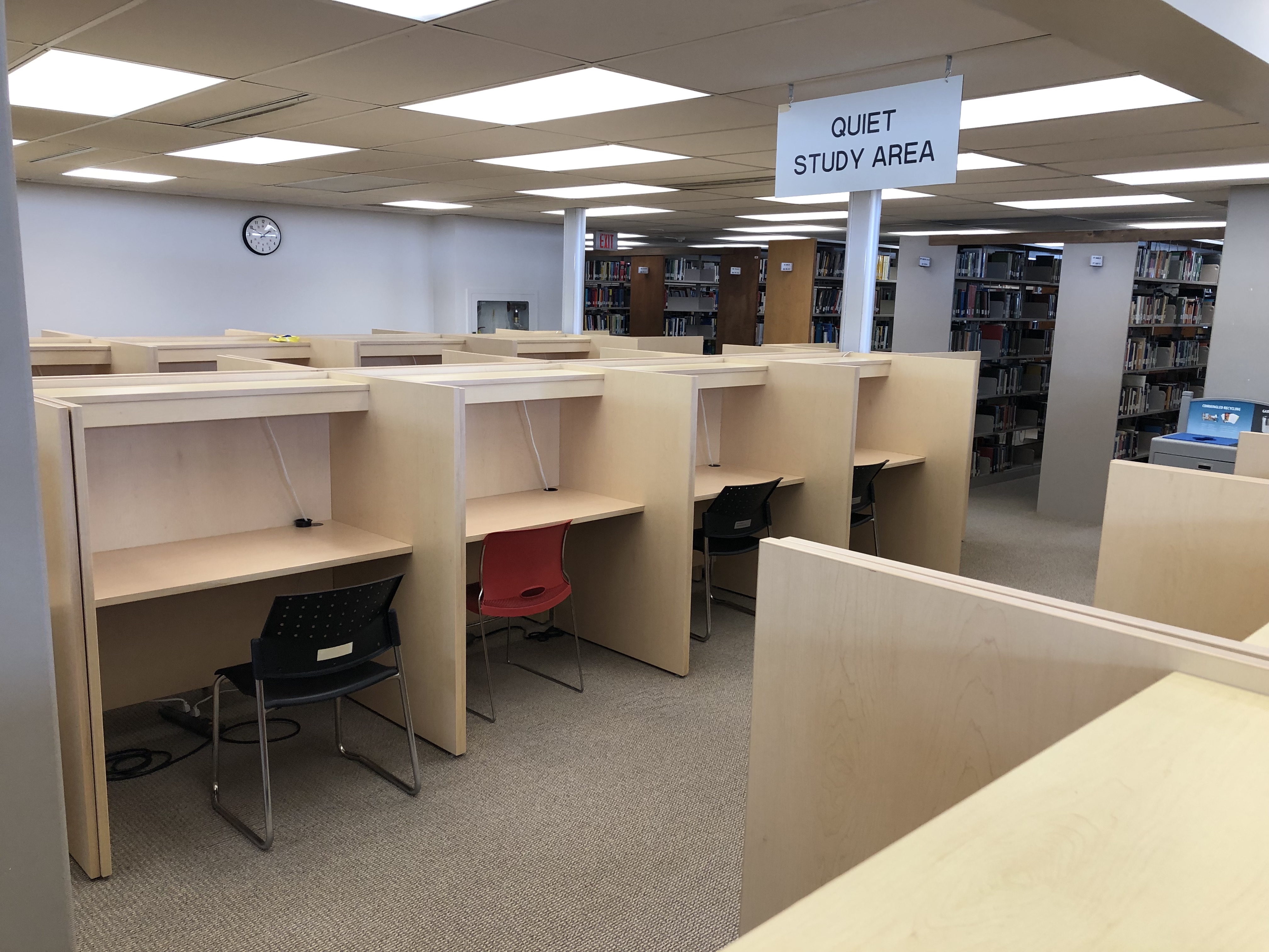 A cluster of about 20 study carrels, grouped into rows of four. The desks surfaces are empty. There are partitions between the desks for privacy. 