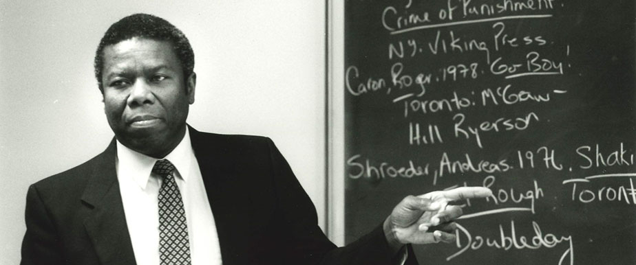 Professor Edcil Wickham wearing a suit pointing at a chalkboard with writing on it.