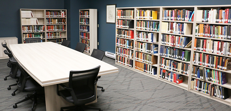 Meeting room with long desk surrounded by chairs. Bookshelves filled with books along the room walls