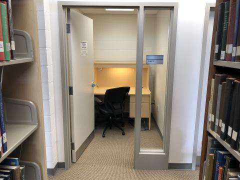 A private study room. There's a desk with large surface and chair. Braille on door signs 