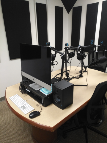 podcast studio desk with an iMac desktop, headsets, and three microphones on articulated arms.  Sound proofing is on the walls.