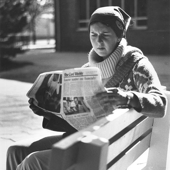 Older black and white photo of person sitting on bench reading the Cord