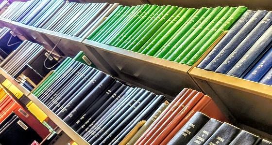 Photo of bound journals in different colours on a shelf in the Library. 