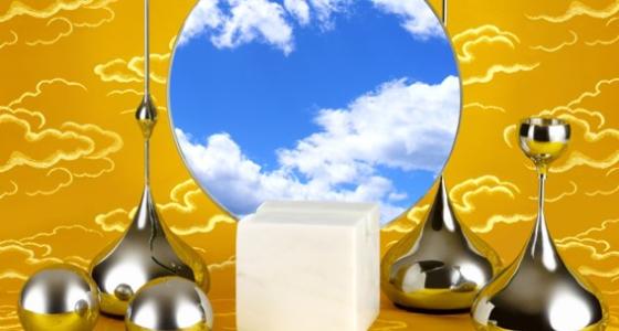 Blue sky and clouds reflected in circular mirror. Next to it are smooth metal tear-shaped structures and in the center is a small even-texture marble cube all on a flat yellow cloud patterned background. 