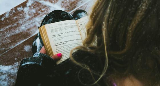 Woman sitting outside on a snowy step reading a book.