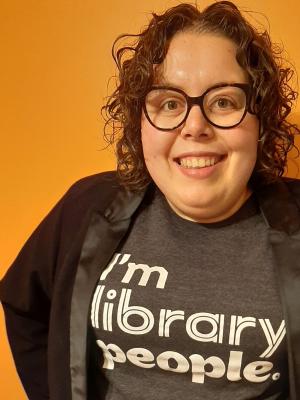 A photo showing Lauren Bourdages against an orange backdrop, her shirt says "I'm Library People"
